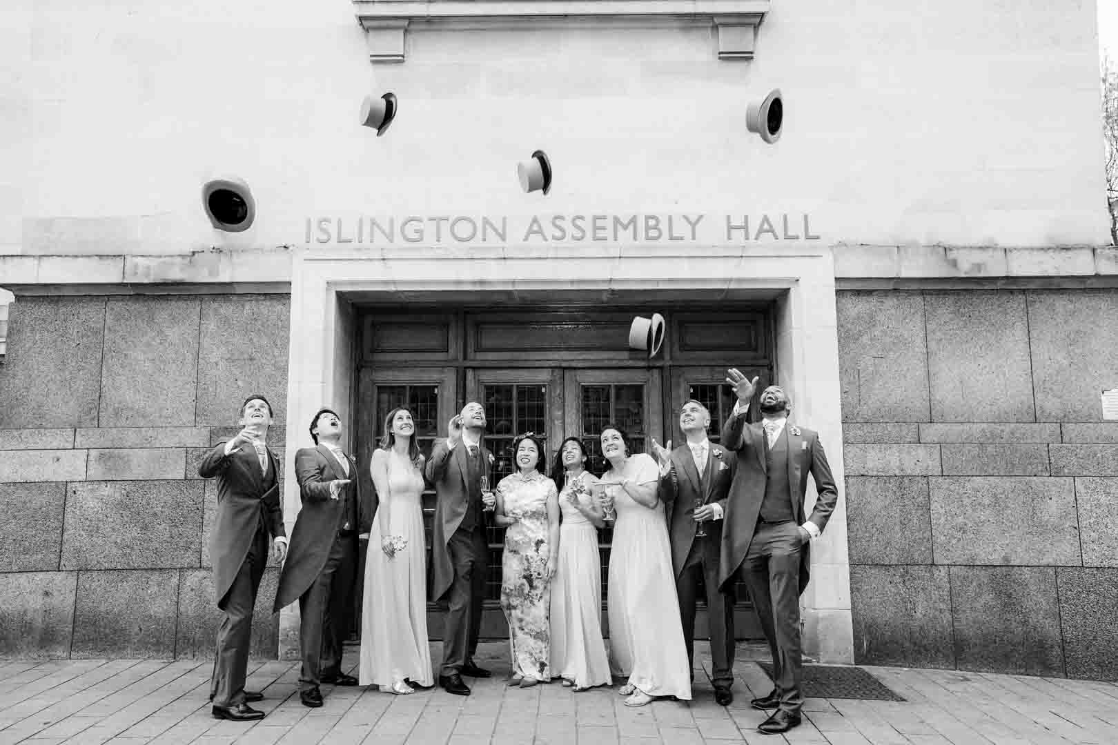 wedding party celebrating outside Islington assembly hall by trowing their top hats in the air