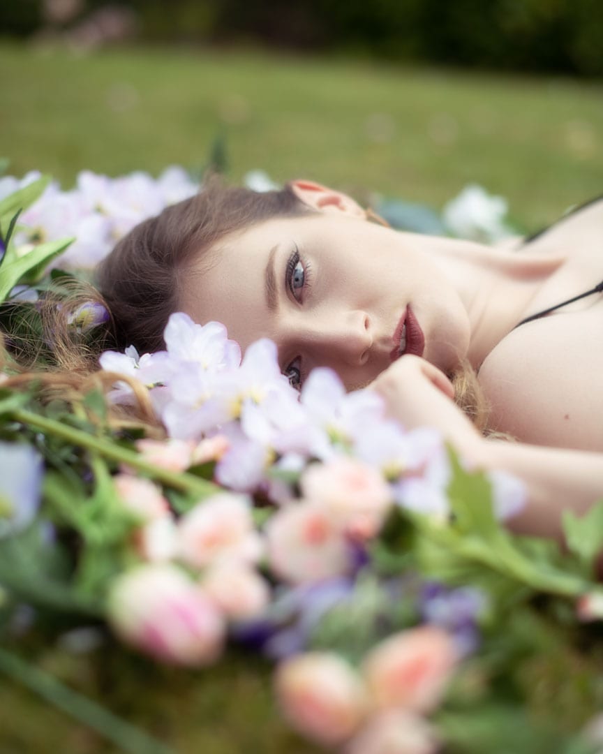 model looking at the camera through flowers laid on the floor