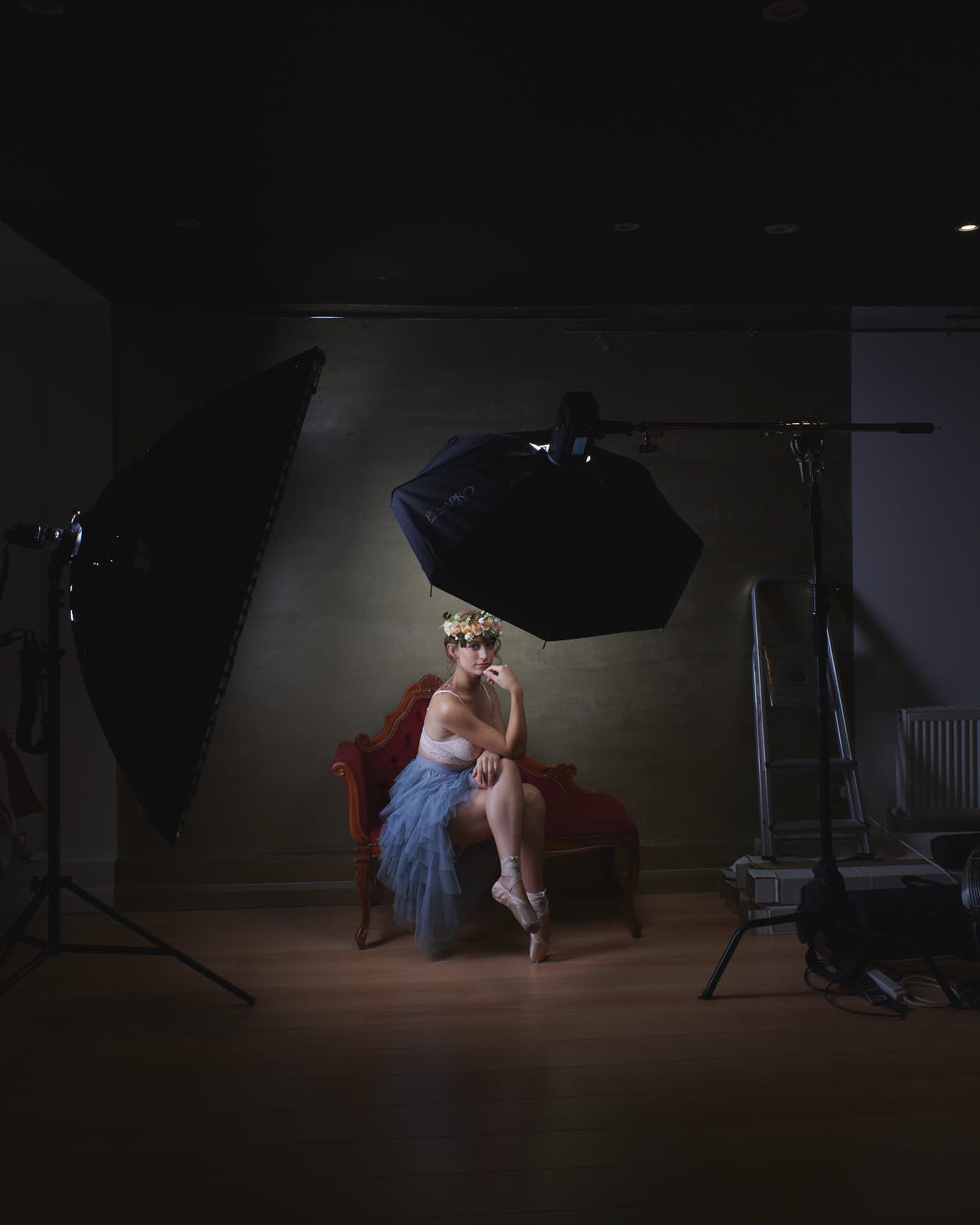 ballet dancer wearing a flower crown sitting on a Chaise lounge surrounded by studio lights
