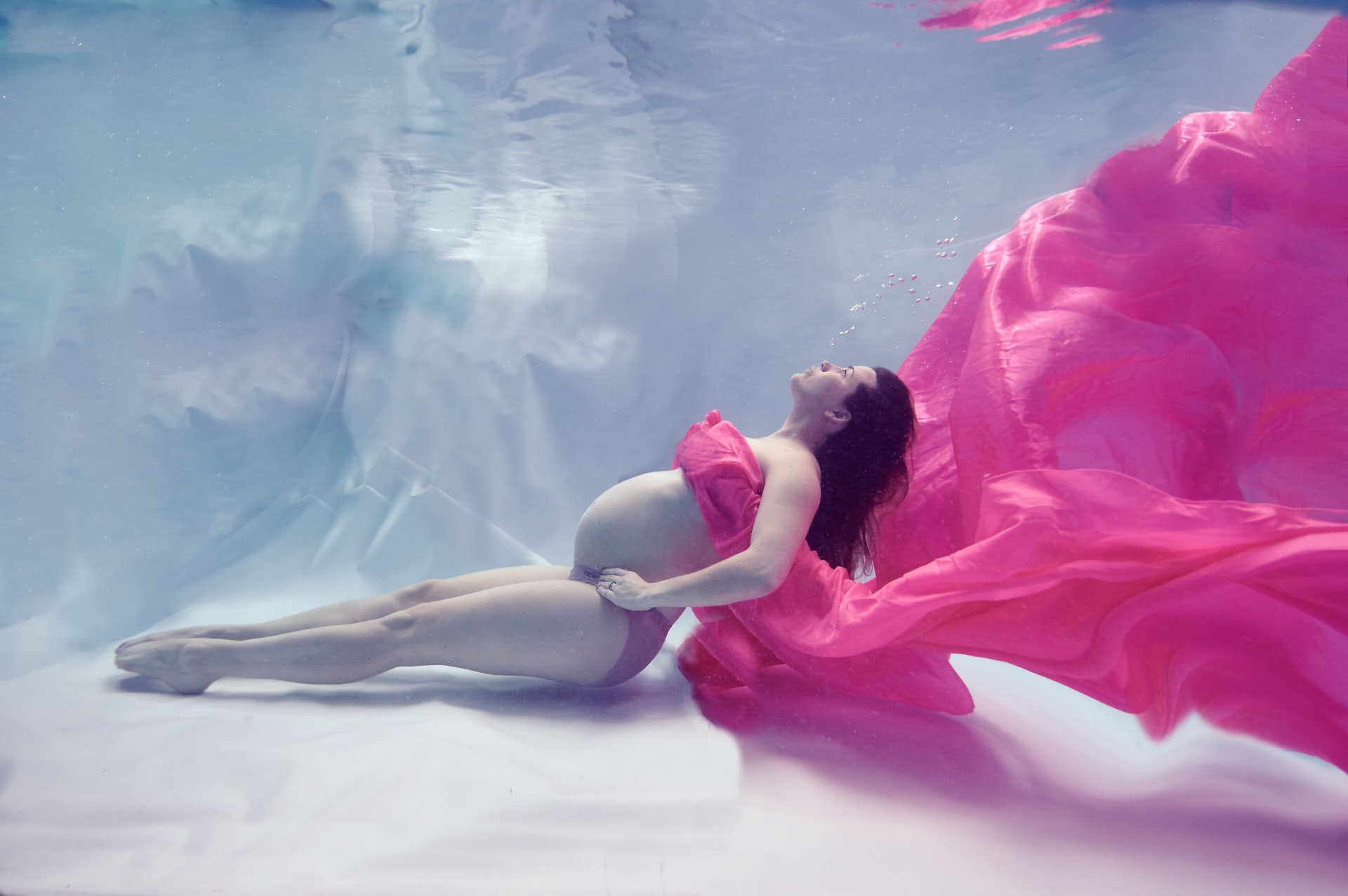 Pregnant lady Underwater covered in pink flowing satin