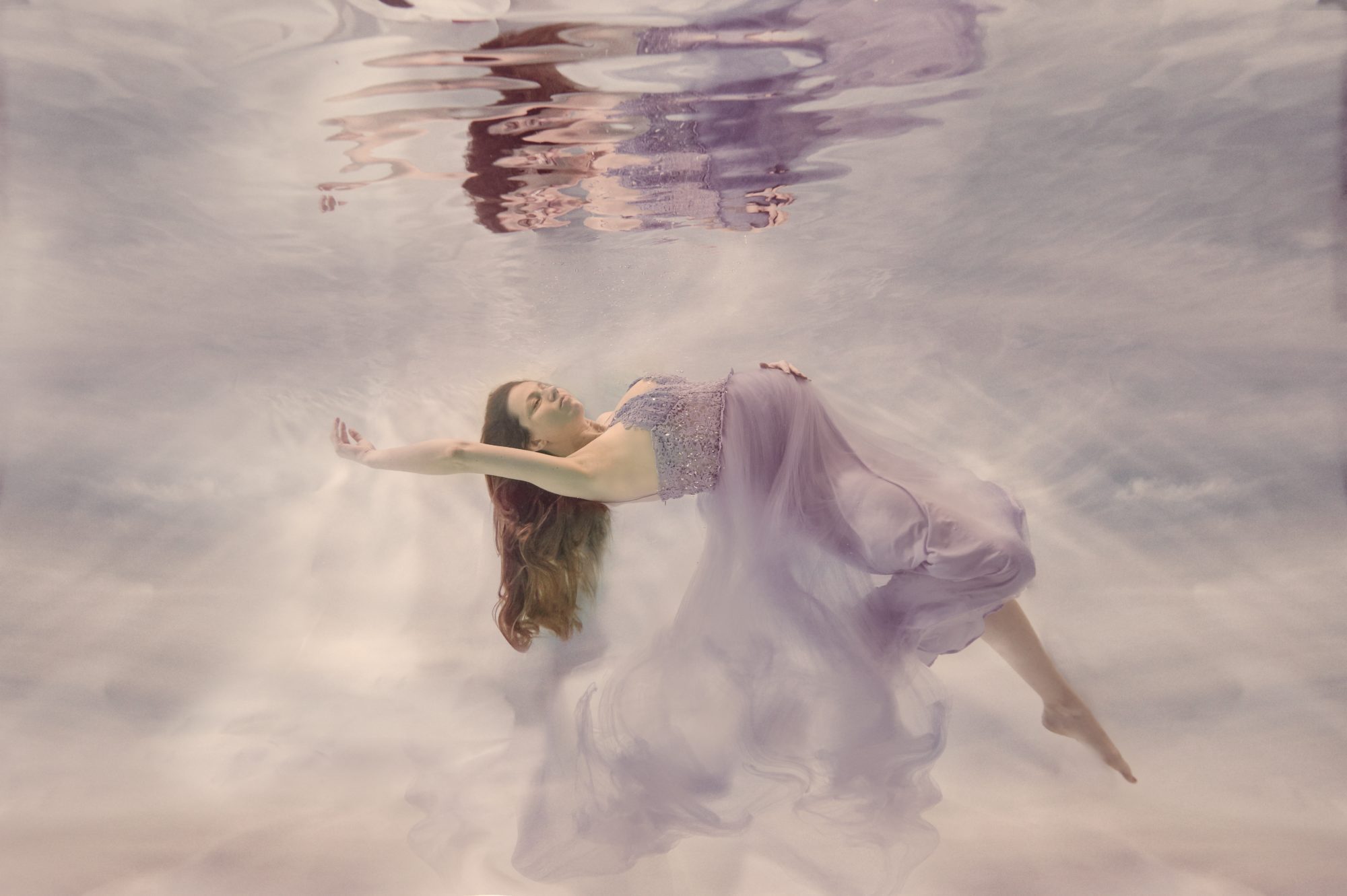 Underwater maternity shoot of a pregnant lady in a lilac dress