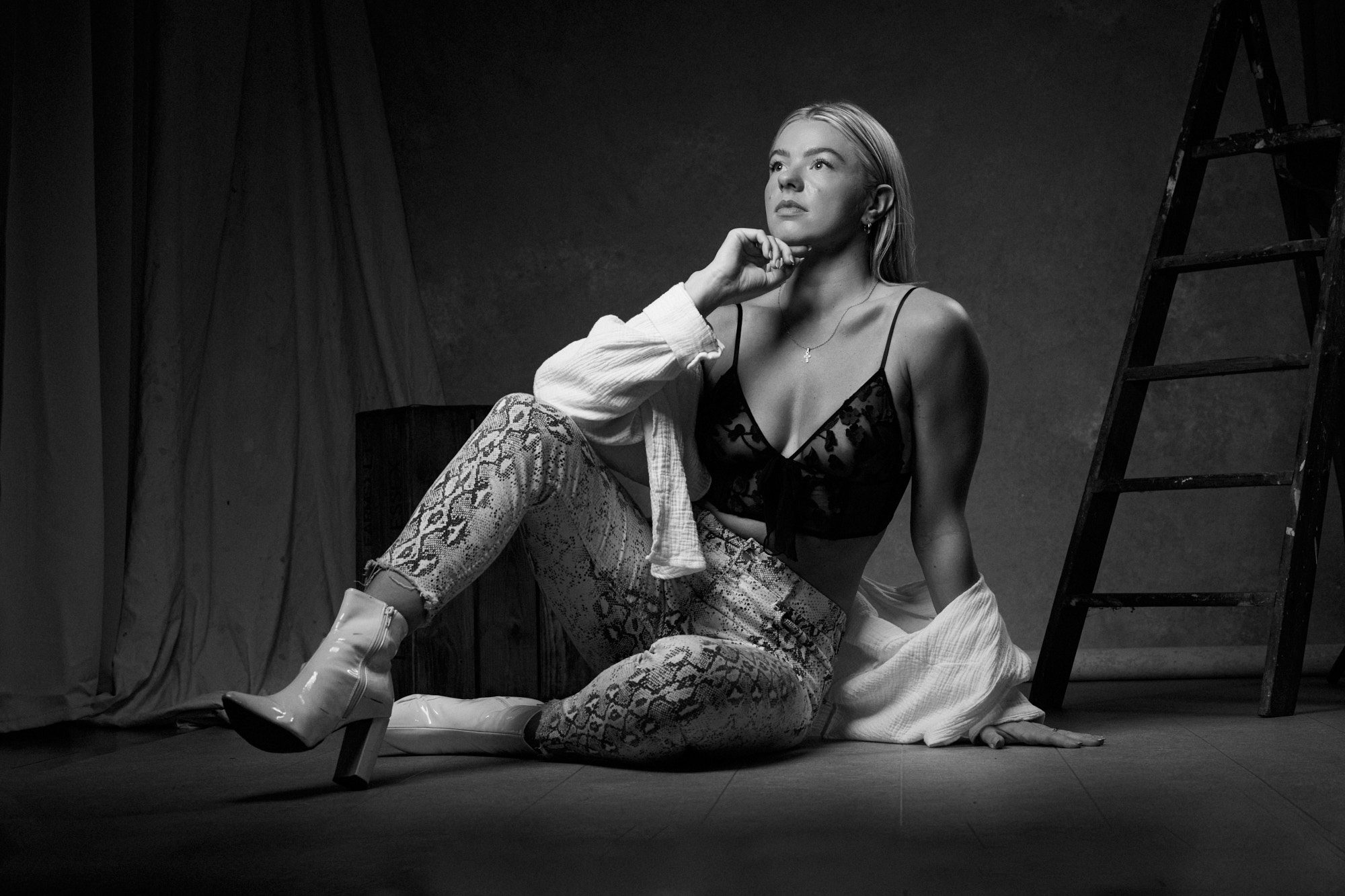 Black and white portrait of model sat on a stool in long leather boots