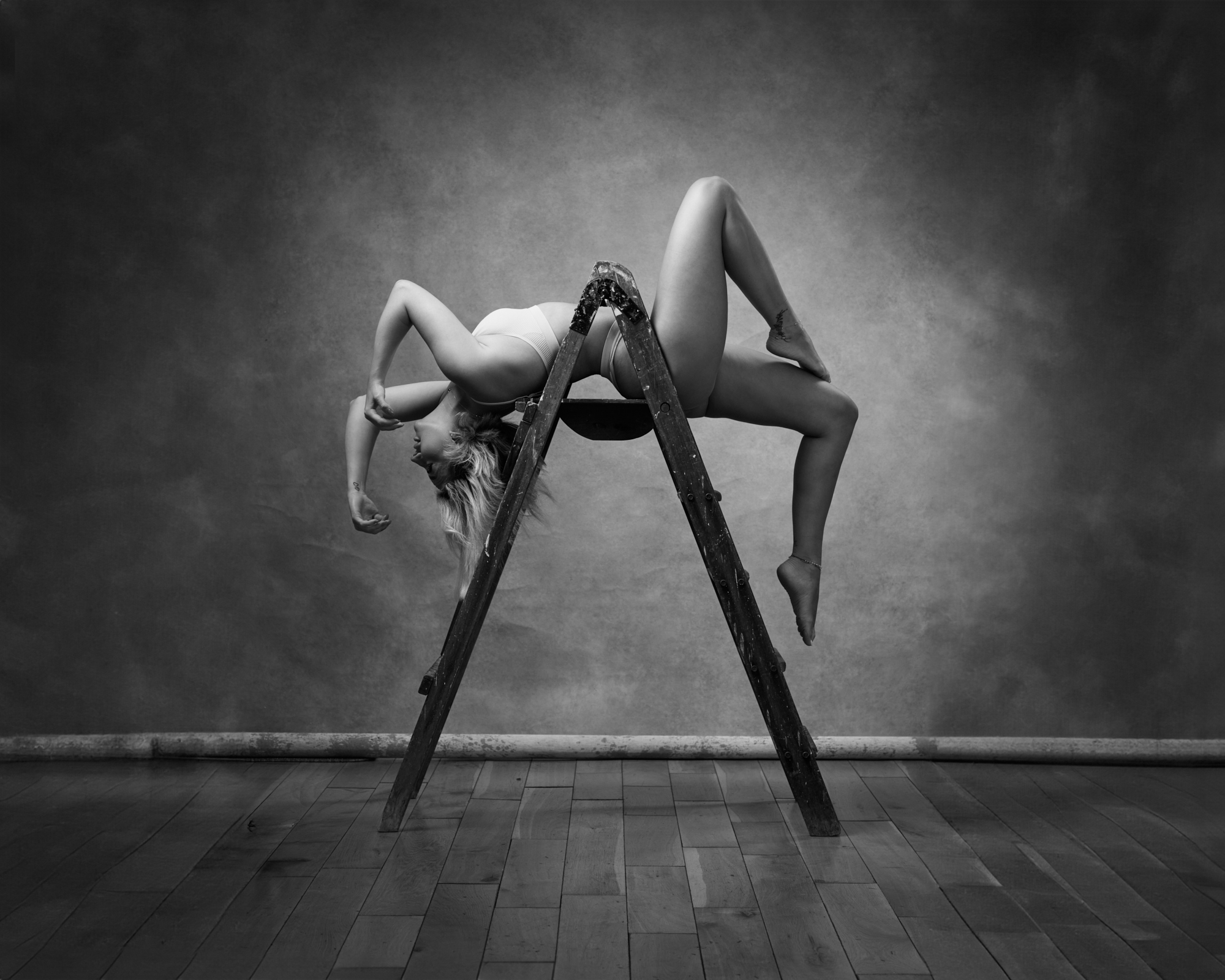 Black and white portrait of model sat on a stool in long leather boots